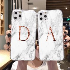 a woman holding up two white marble phone cases with the letter d on them