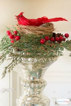 a red bird sitting on top of a glass vase filled with berries and greenery