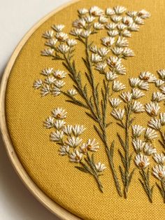 a close up of a embroidery on a yellow cloth with white flowers in the center