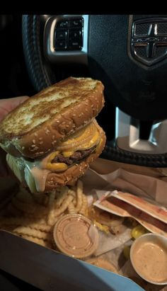 a person is holding up a large sandwich and french fries in front of the car