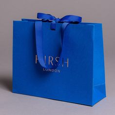 a blue shopping bag with a bow on the front and logo on the back that says hush london