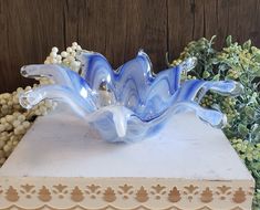 a blue glass sculpture sitting on top of a white box next to flowers and greenery