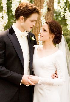 a young man and woman dressed in formal wear standing next to each other near a tree