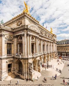 people are walking around in front of an old building with gold statues on the roof