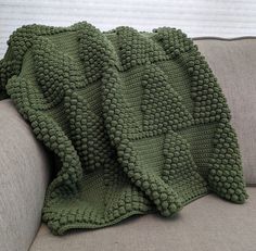 a green crocheted blanket sitting on top of a couch next to a pillow