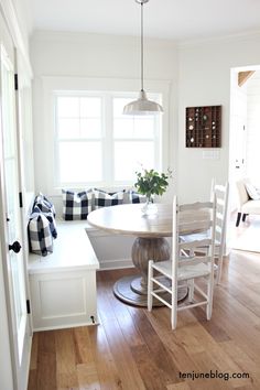 a dining room table and chairs in front of a window with black and white pillows