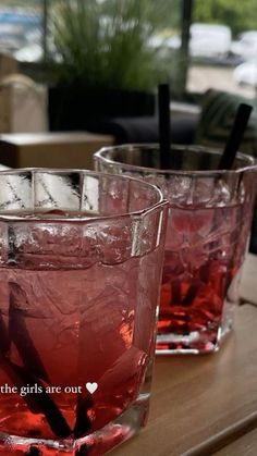 two glasses filled with red liquid sitting on top of a wooden table next to each other