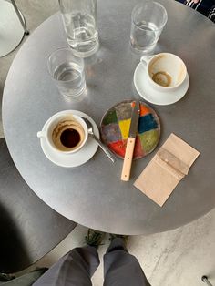 two cups of coffee sit on top of a round table next to some empty glasses