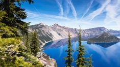 a lake surrounded by trees and mountains under a blue sky with wispy clouds