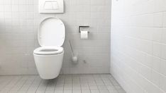 a white toilet sitting in a bathroom next to a urinal and trash can on a tiled floor