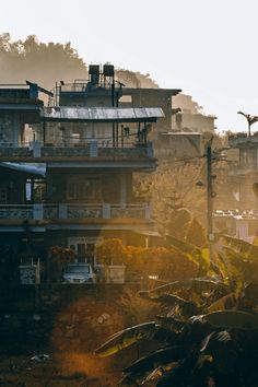 the sun shines brightly in front of some buildings on a hill side with trees and bushes