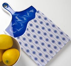 a bowl of lemons next to a cutting board with a blue design on it