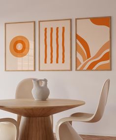 three abstract paintings hang on the wall above a round dining room table with two white chairs