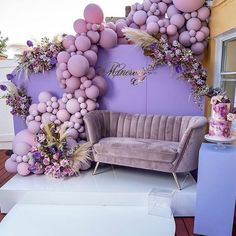 a couch sitting in front of a purple wall with balloons and flowers on it's side