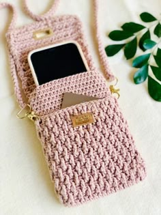 a crocheted pink cell phone case sitting on top of a white surface next to a plant