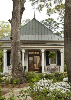 the house is surrounded by white flowers and large trees with blue shutters on each side