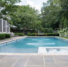 an empty swimming pool surrounded by greenery and trees in the back yard with two lounge chairs on either side