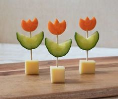 three small pieces of fruit with flowers on them sitting on a cutting board next to cheese cubes