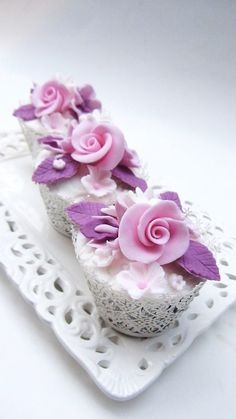 three cupcakes decorated with pink and purple flowers on a white doily plate