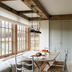 a dining room table and chairs in front of large windows with wooden beams on the ceiling