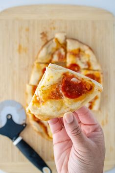 someone holding up a slice of pizza on a cutting board