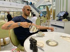 a man sitting at a table with a cup and saucer in his hand as he pours coffee