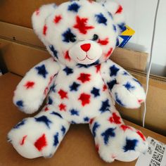 a red, white and blue teddy bear sitting on top of a cardboard box