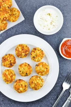 a white plate topped with crab cakes next to a bowl of ketchup and a fork