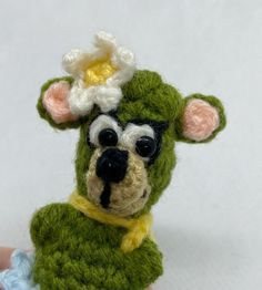 a hand holding a small crocheted mouse with a flower on it's head