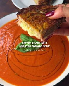 someone is holding up a piece of bread over a bowl of tomato soup