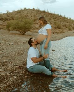 a pregnant woman sitting on the ground next to a man who is holding her belly