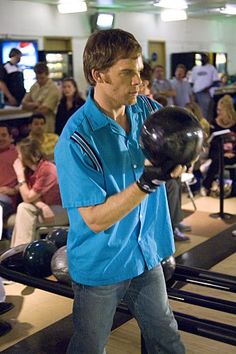 a man holding a bowling ball in his hand while standing next to other people watching