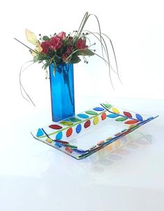 a blue vase filled with red flowers on top of a glass plate next to a flower arrangement