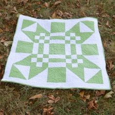 a green and white quilt sitting on top of some leaves in the grass with it's diagonal design