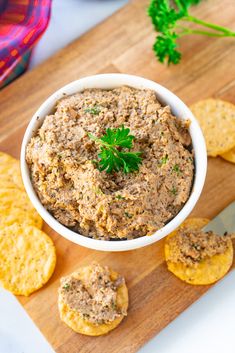 a white bowl filled with dip next to crackers and parsley on a cutting board