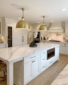 a large kitchen with white cabinets and gold pendant lights above the island countertop, along with an oven