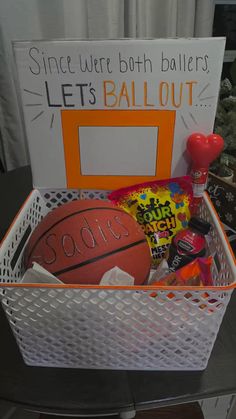 a white basket filled with lots of different types of sports items and candy in front of a sign that says let's ball out