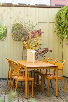 a wooden table and chairs in front of a yellow wall with potted plants on it