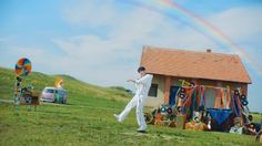 a man standing in front of a house with a rainbow in the sky behind him