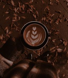 a cappuccino in a black cup on top of a table with leaves around it