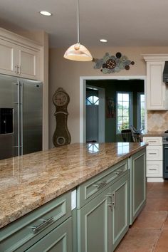 a kitchen with green cabinets and marble counter tops, an island in the middle has a clock on it