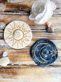 two ceramic plates sitting on top of a wooden table next to a white flower and some other items