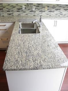 a kitchen with white cabinets and granite counter tops, along with an island style sink