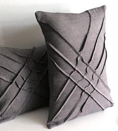 two gray pillows sitting next to each other on top of a white table and one has a knoted design on it