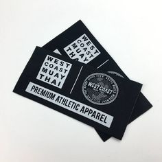 two black stickers with white writing on them and some type of label that says west coast muay thaay premium athletic apparel