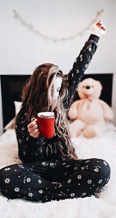 a woman with long hair sitting on a bed holding a cup