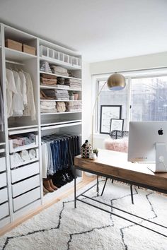 a computer on a desk in front of a large closet with clothes and other items