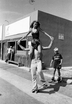 a woman riding on the back of a skateboard next to a man standing in front of a building