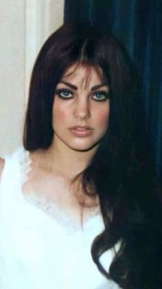 a woman with long dark hair and blue eyes posing for a photo in front of a curtain