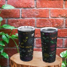 two black tumblers sitting on top of a wooden stump next to a brick wall